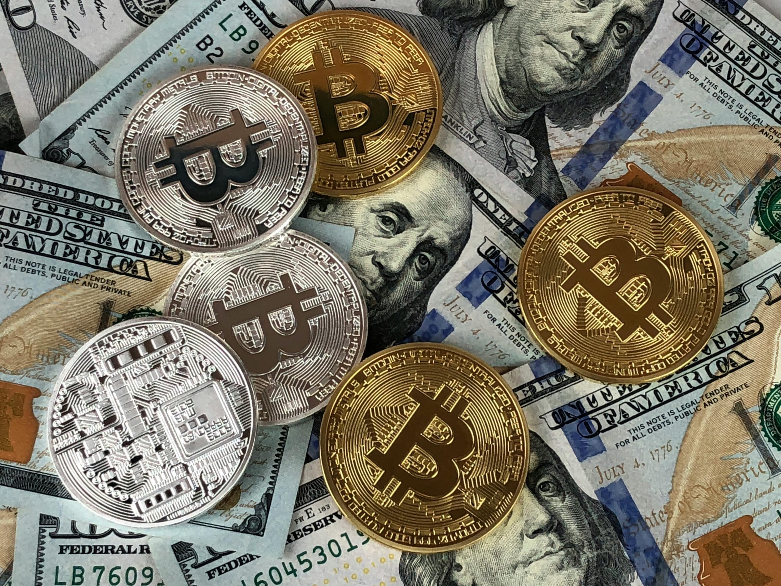 Monedas físicas de Bitcoin doradas y plateadas sobre billetes de cien dólares estadounidenses.